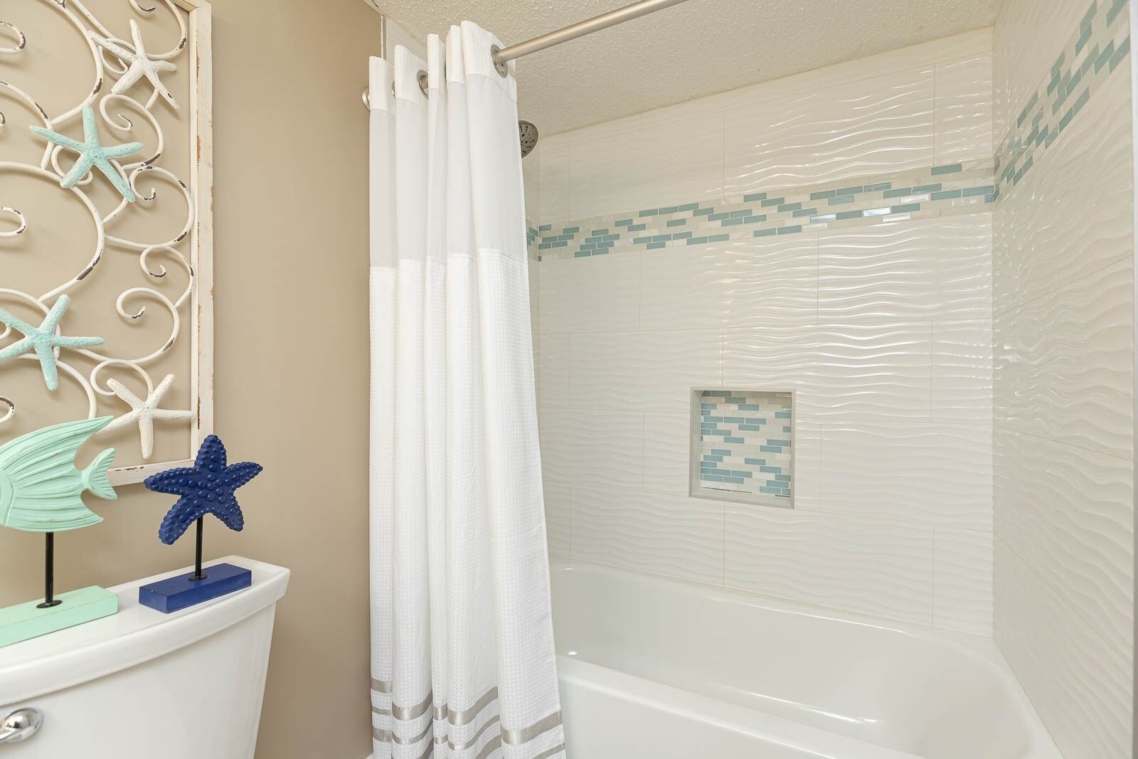 Une salle de bain avec une douche, des toilettes et un mur décoratif orné d’étoiles de mer et d’un poisson.