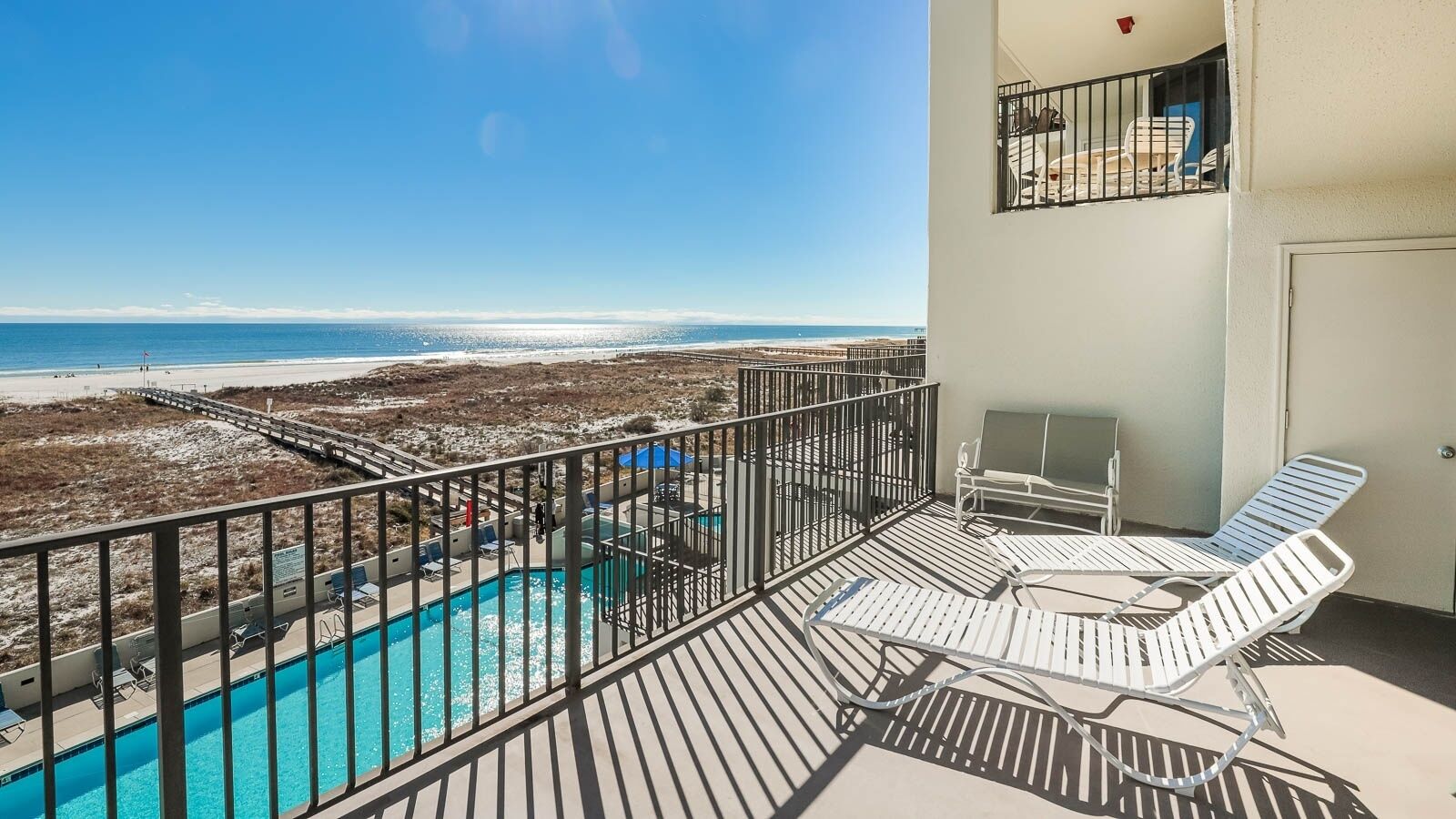 Un balcon avec une piscine, des chaises longues et une vue sur la plage.