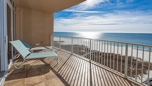 A balcony with two lounge chairs, a view of the ocean, and a sandy beach.