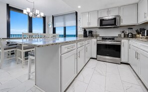 A modern kitchen with white cabinets, a large island with seating, a built-in oven, and a view of the ocean. - Phoenix Vii 7401 3 Bedroom Condo (Orange Beach)
