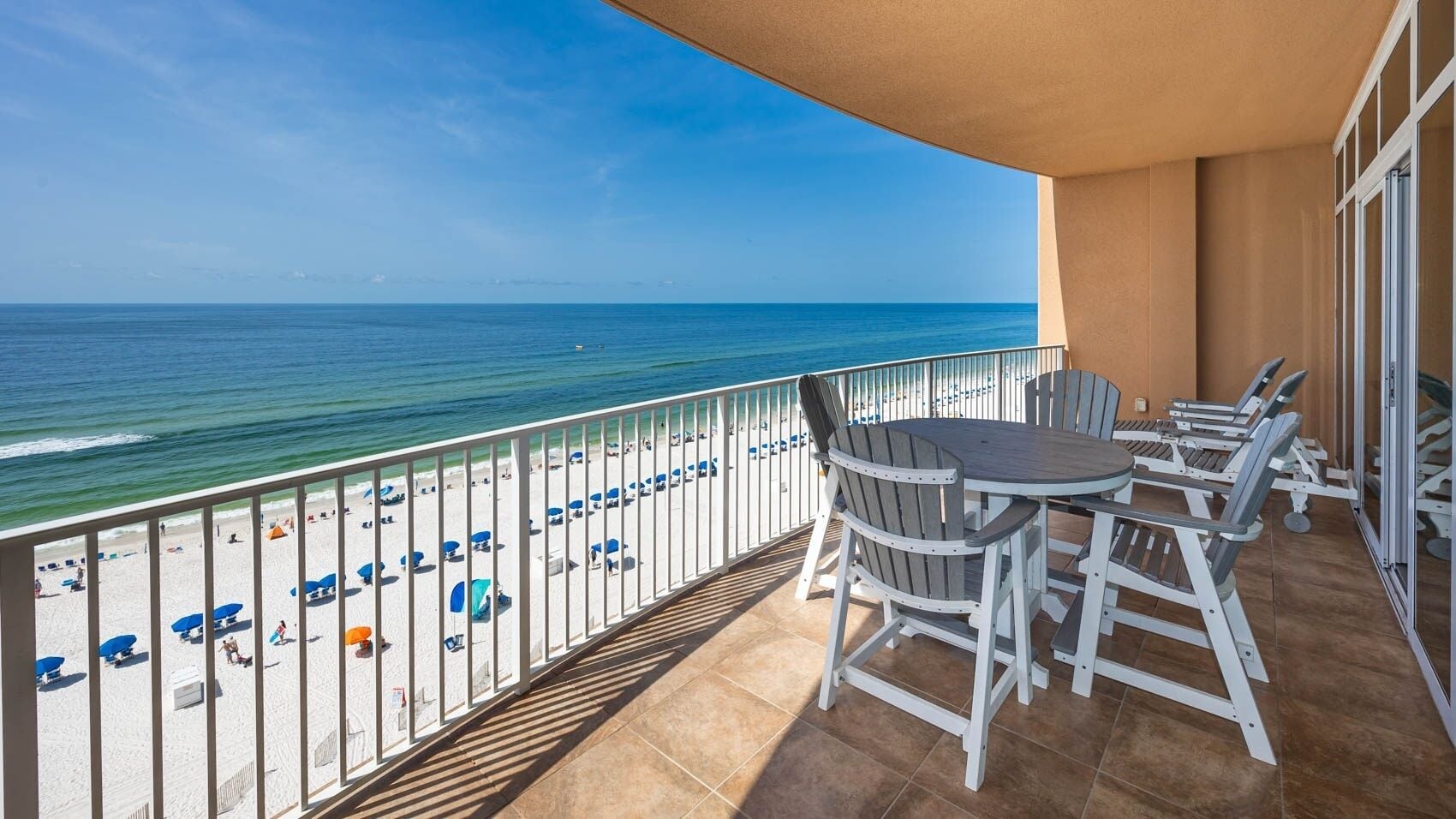A balcony with a view of the beach and ocean, equipped with a table and chairs.