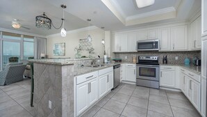 A modern kitchen with white cabinetry, a granite countertop, stainless steel appliances, and a large island with a built-in sink.