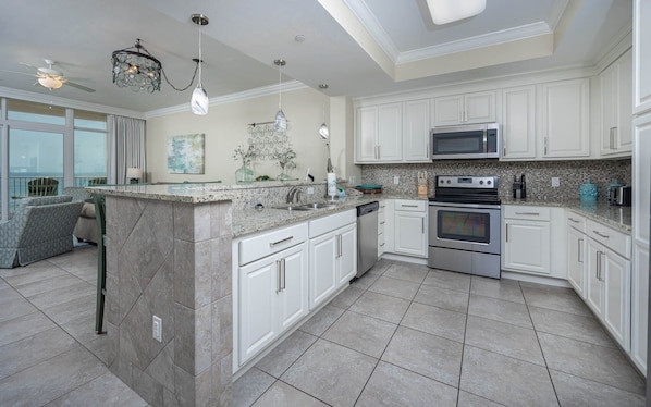 A modern kitchen with white cabinetry, a granite countertop, stainless steel appliances, and a large island with a built-in sink. - Phoenix Gulf Shores 702 3 Bedroom Condo (Gulf Shores)