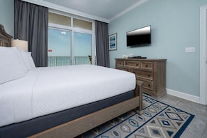 A bedroom with a large bed, a dresser, a flat-screen TV, and a balcony with curtains. - Phoenix Gulf Shores 702 3 Bedroom Condo (Gulf Shores)