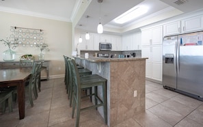 A modern kitchen with white cabinets, a stainless steel refrigerator, a microwave, and a granite countertop. - Phoenix Gulf Shores 702 3 Bedroom Condo (Gulf Shores)