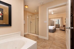 Une salle de bain d’hôtel avec une baignoire, un espace de douche vitré et un lit dans la pièce adjacente.