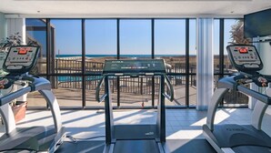 A gym with treadmills and a stationary bike, large windows with a view of the beach.