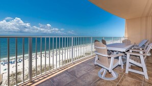 A balcony with a view of a beach, a table, and chairs.