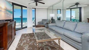 A hotel room with a balcony, a sofa, a coffee table, and a desk.