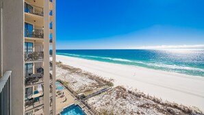 A beachfront hotel with balconies overlooking the ocean, a pool, and a sandy beach.