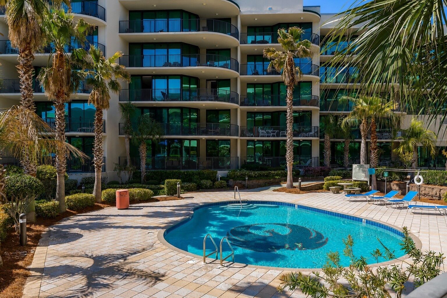 A hotel with a pool, palm trees, and a multi-story building with balconies.