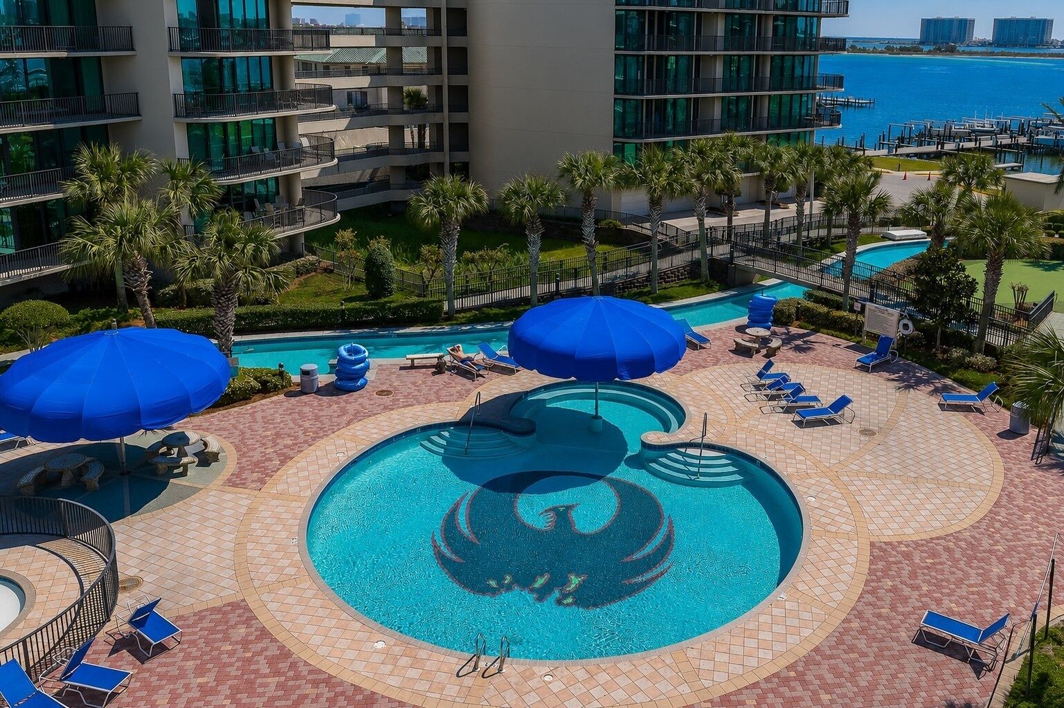 A rooftop pool with blue umbrellas, lounge chairs, and a view of the ocean.