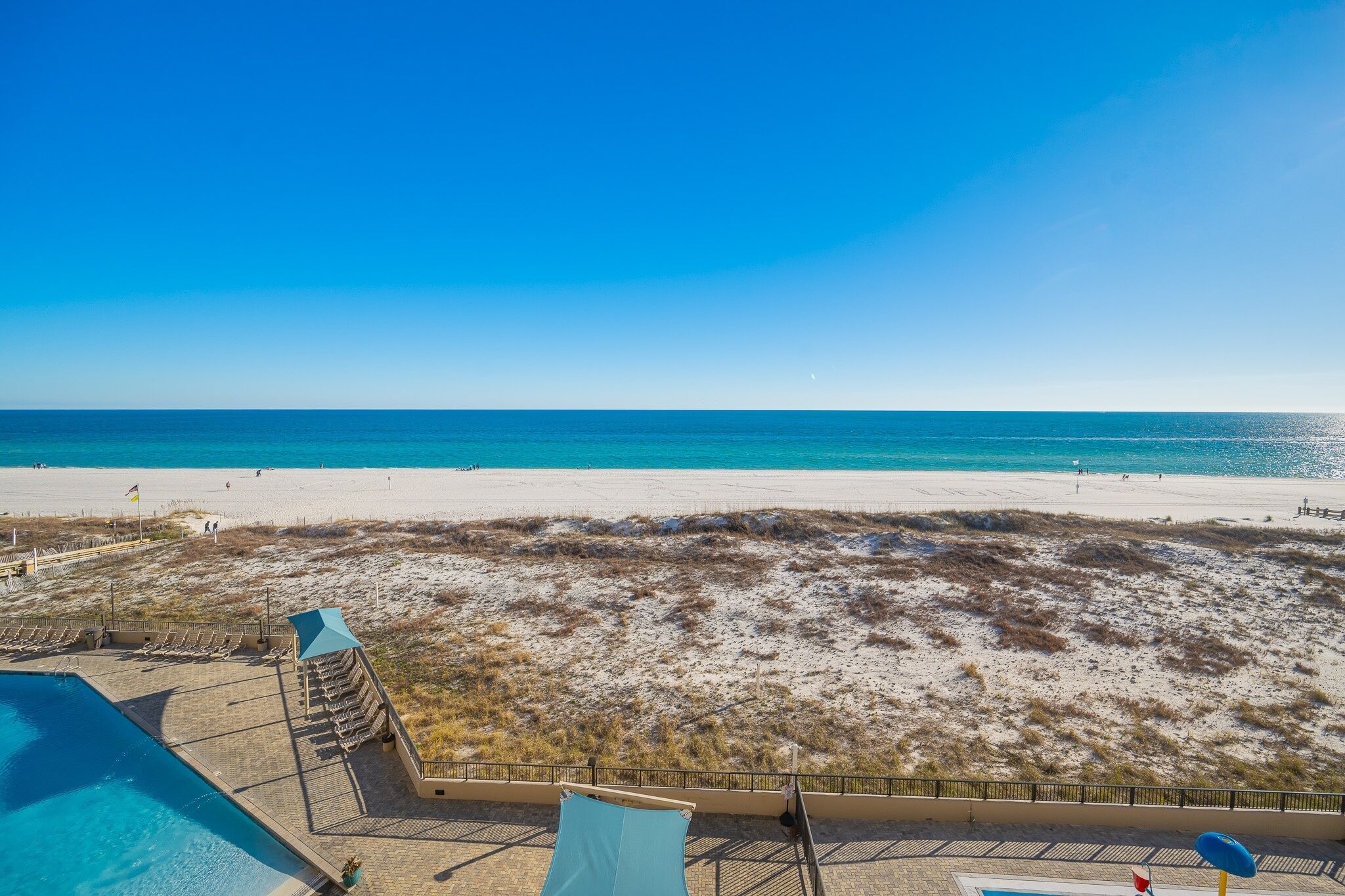A beach view with a pool area and lounge chairs.