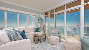 A spacious balcony with a view of the city skyline, furnished with a white sofa, a round wooden table, and a light blue armchair. - Phoenix Orange Beach Ii 1705 4 Bedroom Condo (Orange Beach)