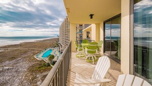 Un balcon avec vue sur la plage et la piscine, des chaises blanches et une table.
