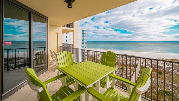 Un balcon avec une table et des chaises, donnant sur une plage et l’océan.