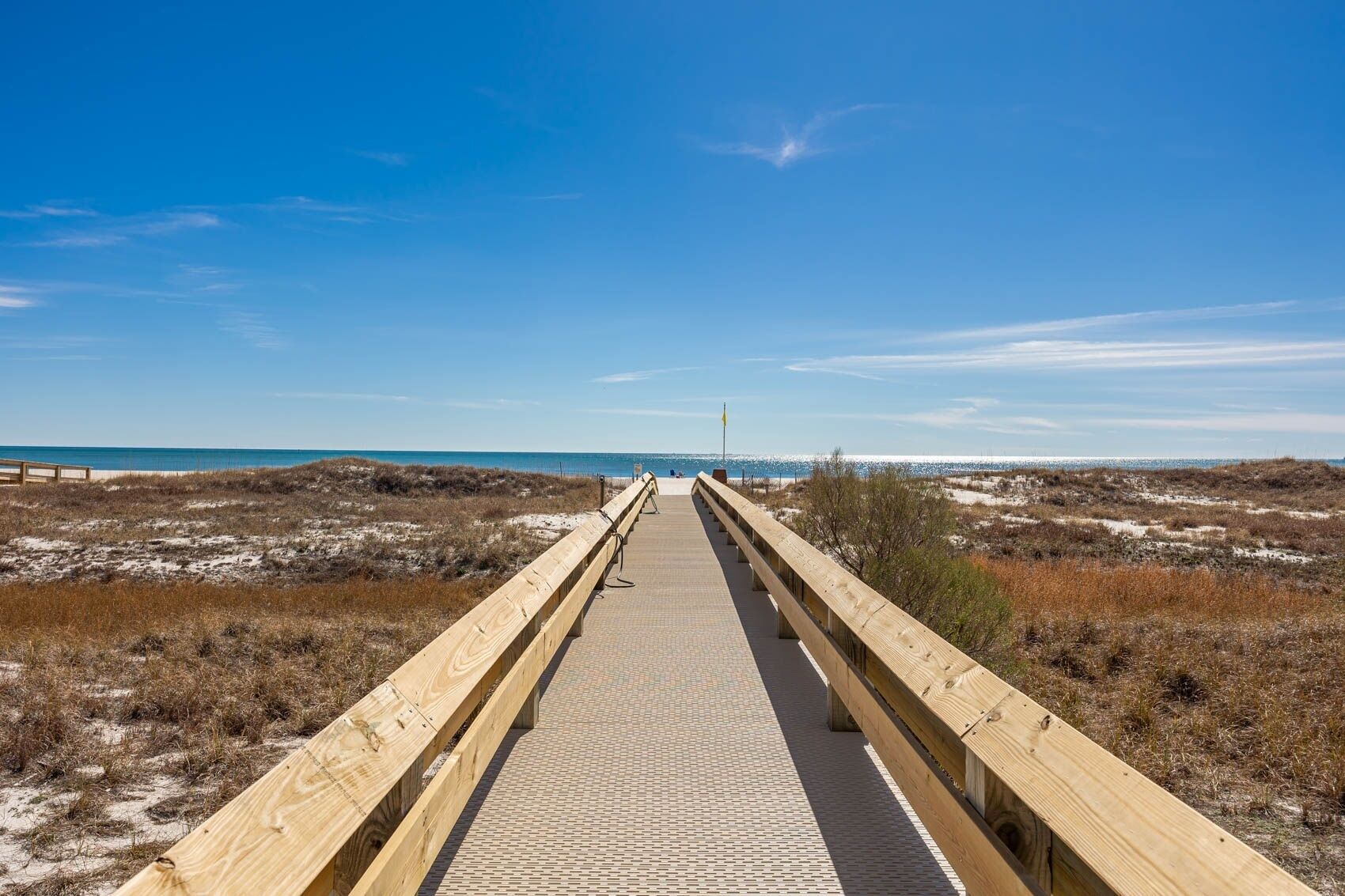 En träpromenad som leder till en strand med klar himmel.