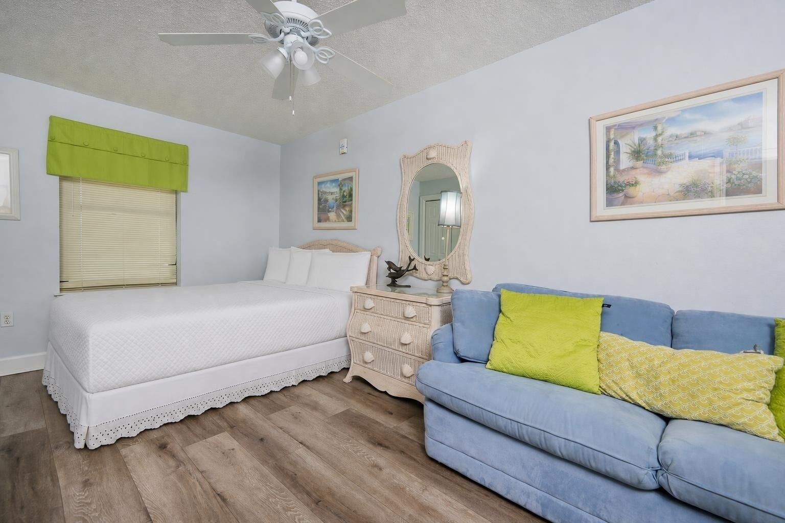 A bedroom with a bed, a dresser, a blue sofa, a ceiling fan, and a framed picture on the wall.