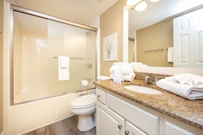Bathroom features a glass-enclosed shower, white toilet, and granite countertop with sink.