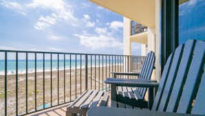 A balcony with two Adirondack chairs and a table, overlooking a beach with a clear sky. - Phoenix Vii 7612 3 Bedroom Condo (Orange Beach)
