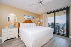 A hotel room with a large bed, two bedside tables with lamps, a ceiling fan, and a view of the beach through a sliding glass door. - Phoenix Vii 7612 3 Bedroom Condo (Orange Beach)