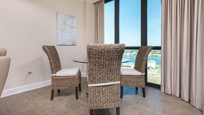 Een kamer met twee rieten stoelen, een klein rond tafeltje en uitzicht op de zee door grote ramen.