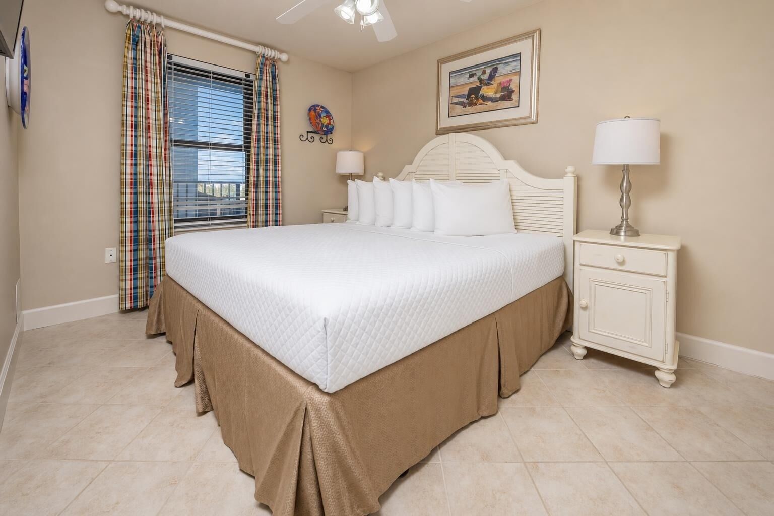 A bedroom with a bed, a nightstand, a lamp, a window with curtains, and a wall-mounted picture.