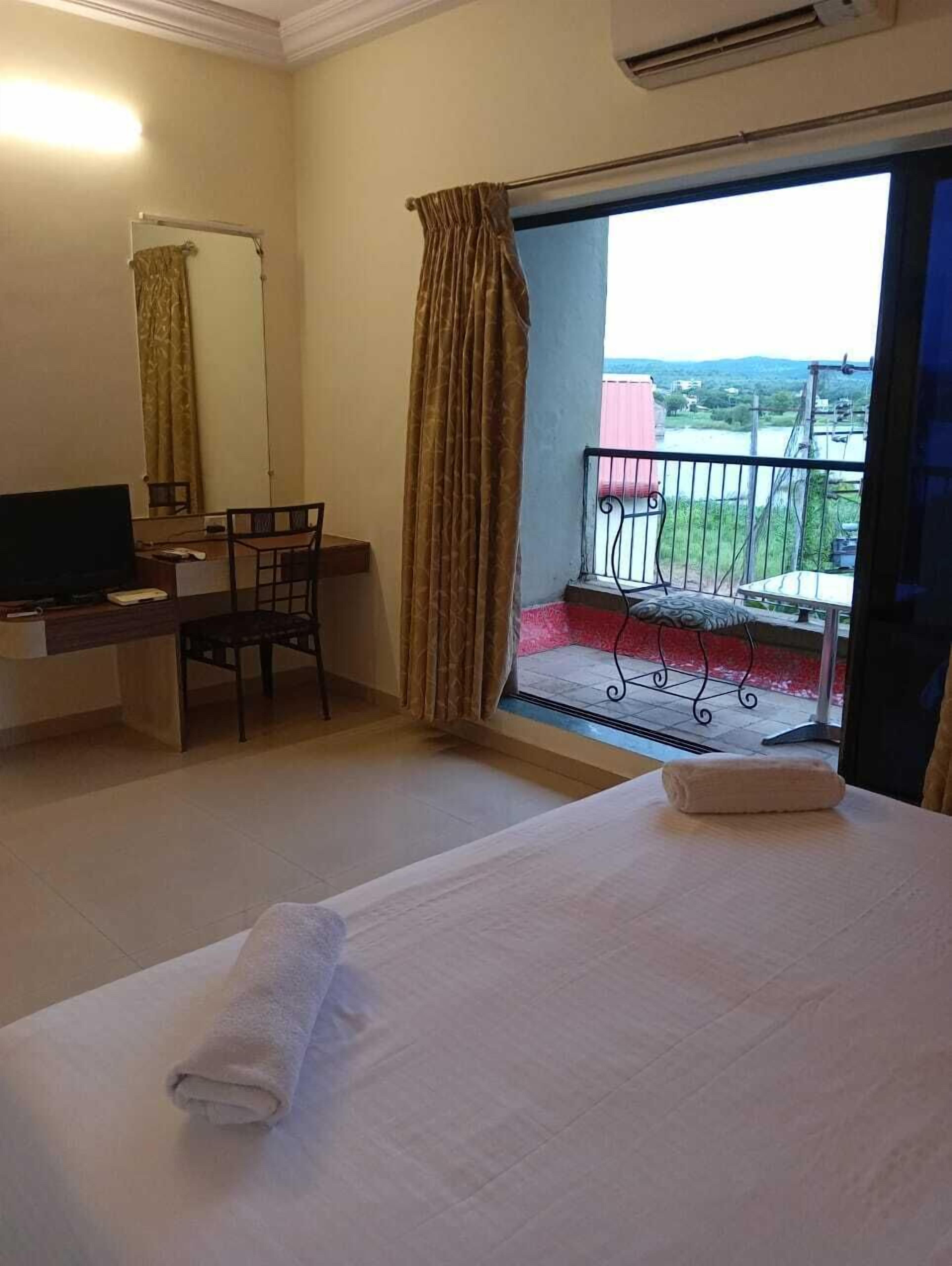 Habitación de hotel con cama, escritorio con silla, televisor y balcón con vistas al paisaje.