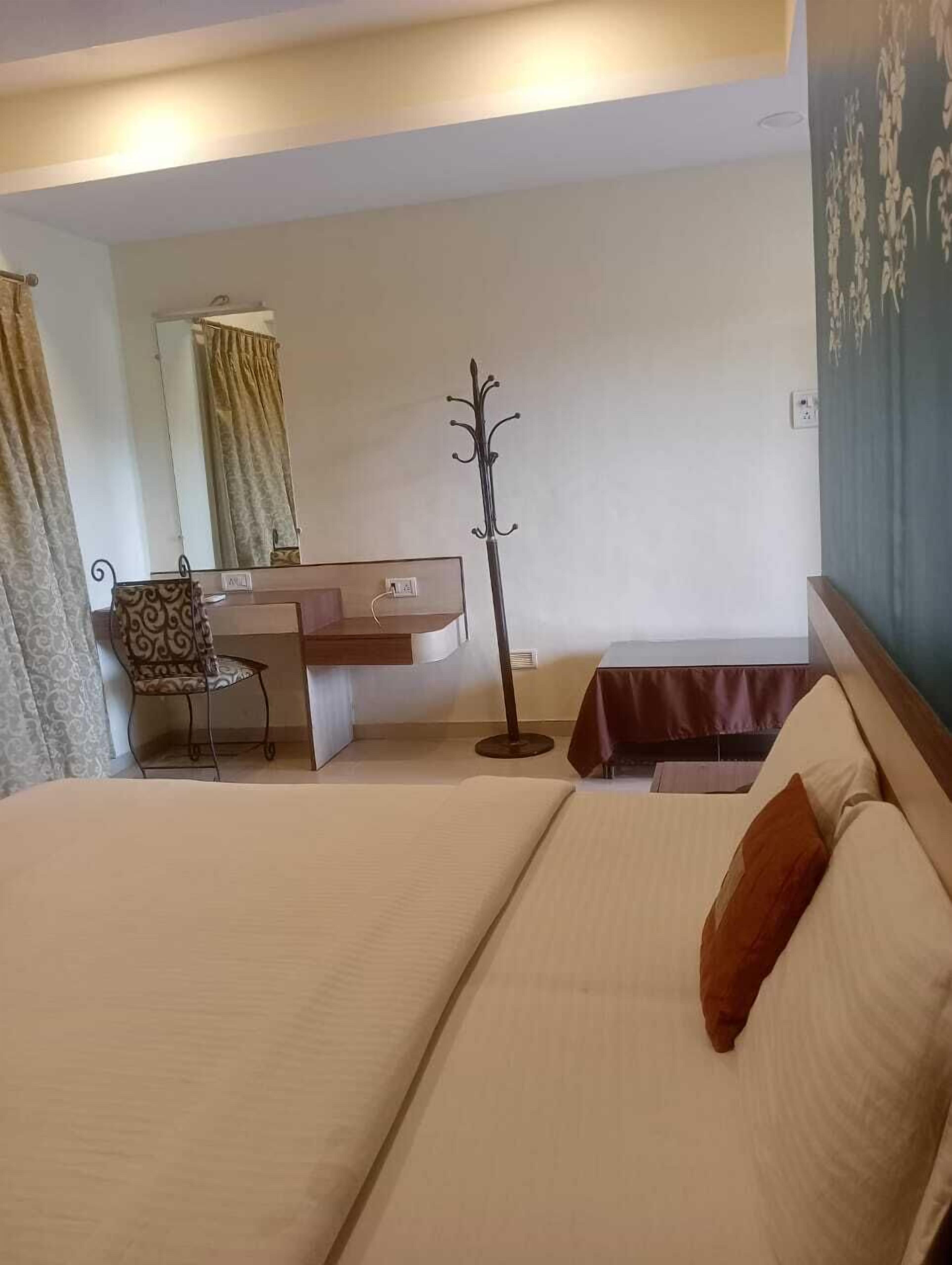 Habitación de hotel con cama, escritorio, silla, perchero y espejo.