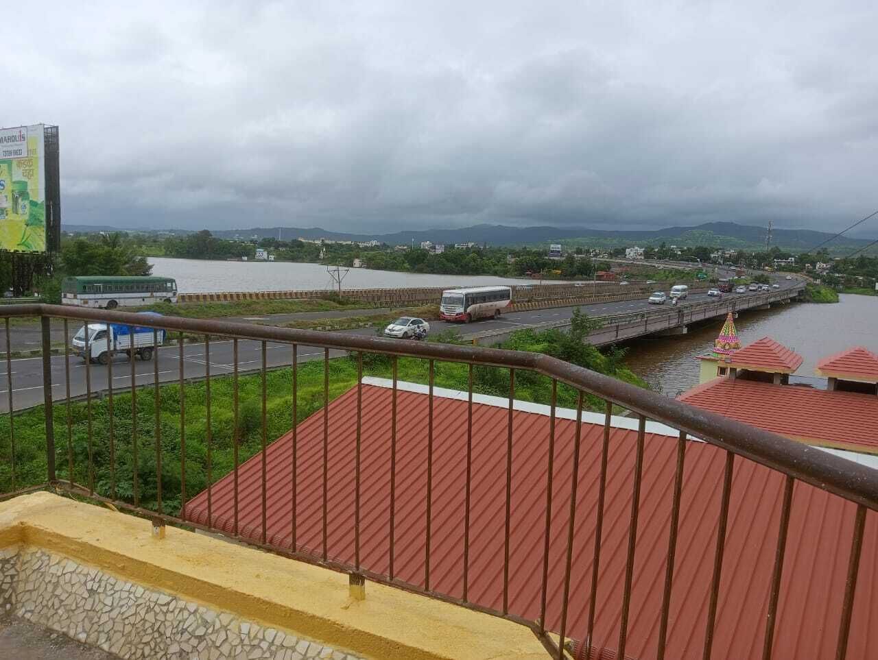 Vista desde un balcón con un puente, un río y colinas distantes bajo cielos nubosos.