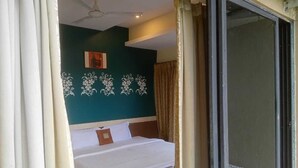 A bedroom with a bed, a ceiling fan, and a view through a glass door. - Hotel Vegas (Khandala)