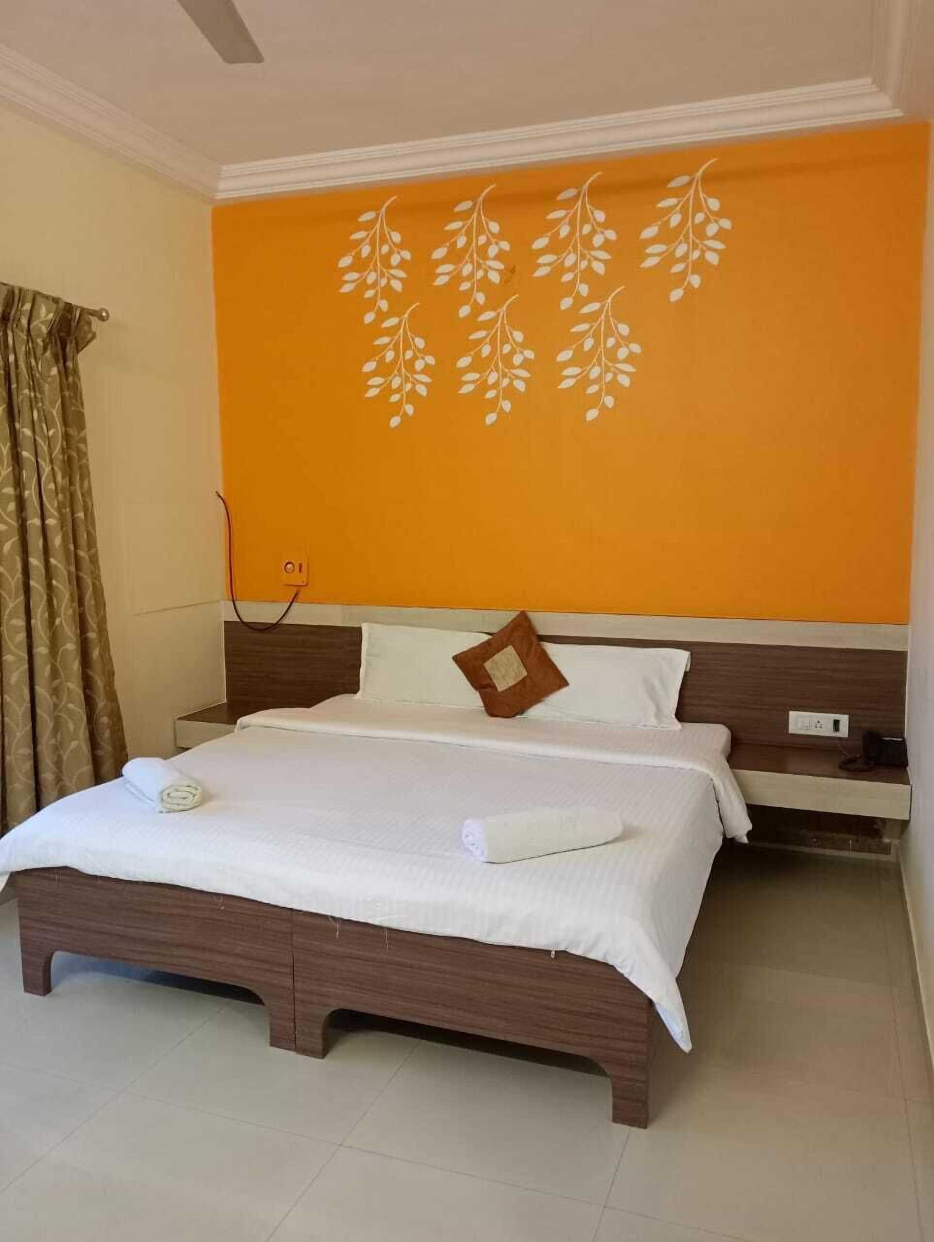 A hotel room with a bed, a nightstand, and a wall with a leaf pattern.