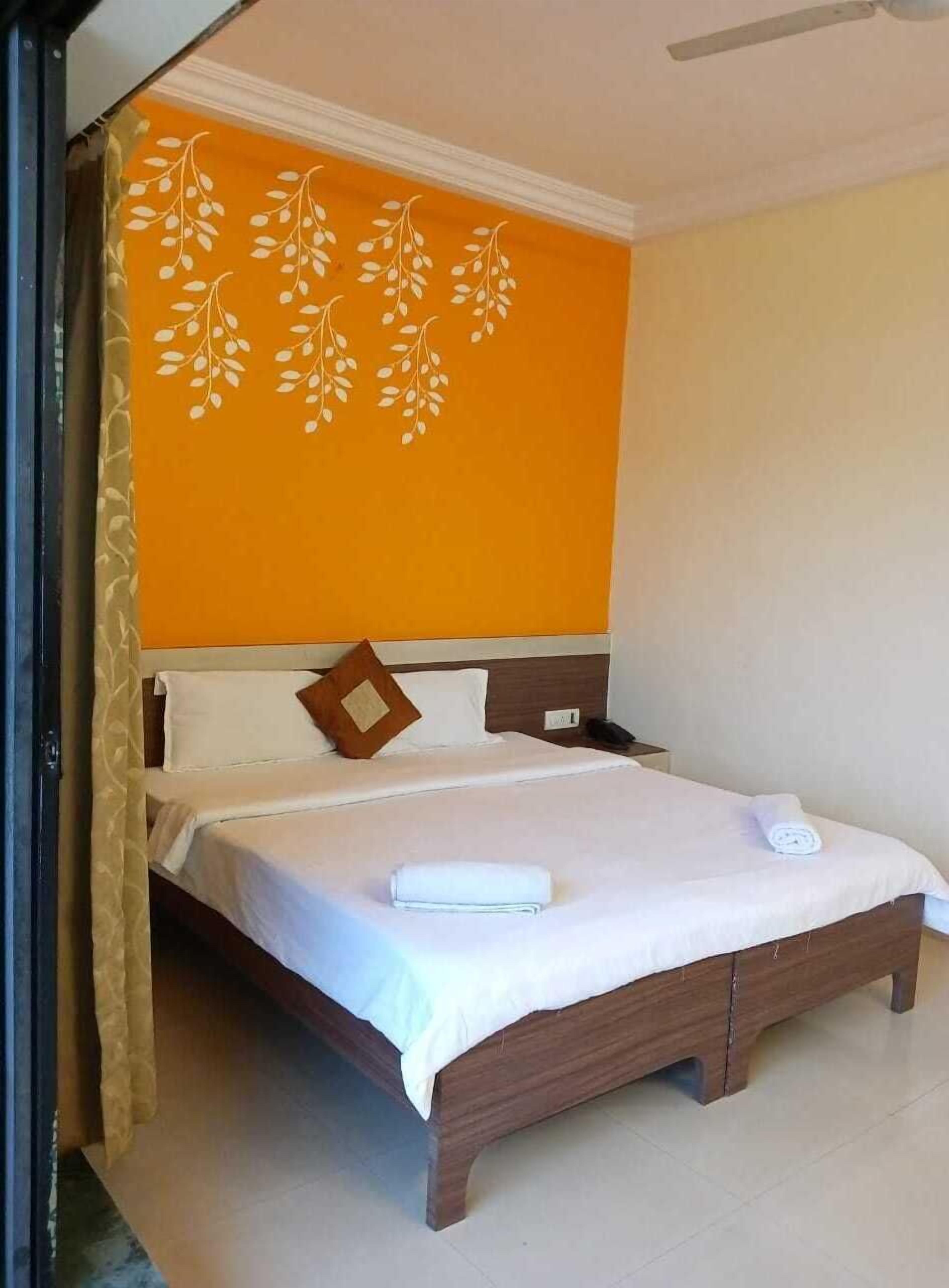 A hotel room with a bed, a headboard, a wall with a leaf pattern, and a curtain.