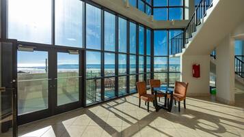 A spacious room with large floor-to-ceiling windows offering a view of the beach and ocean.