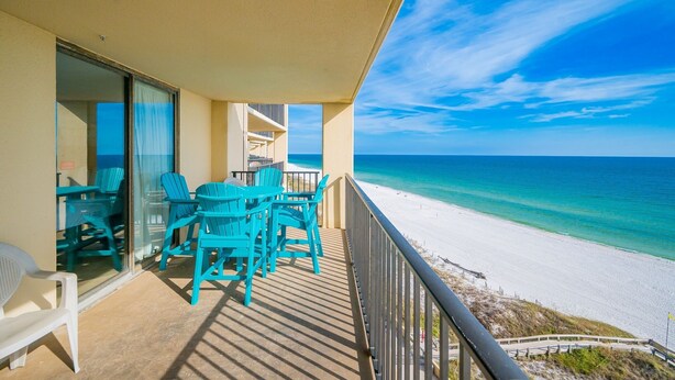 Ein Balkon mit türkisfarbenen Stühlen und einem Tisch mit Blick auf einen Strand.