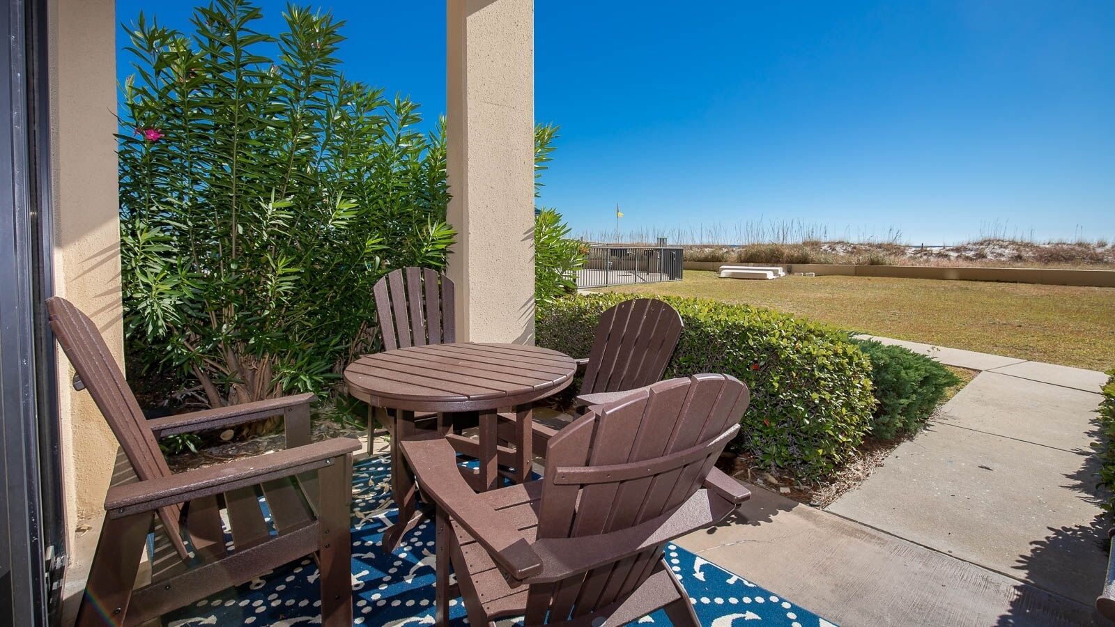 A patio with a round table and four Adirondack chairs, surrounded by greenery and a clear view of the landscape.