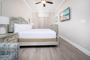 Ein Schlafzimmer mit einem Bett, einem Deckenventilator, einem Nachttisch, einer Kommode, einem Sessel und einem Bild an der Wand.