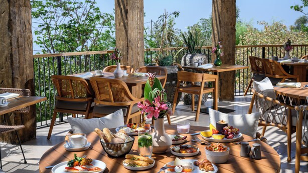 An outdoor dining area with wooden tables and chairs, surrounded by trees and plants. - Canaan Hotel - Limited Edition By Fattal (Safed)