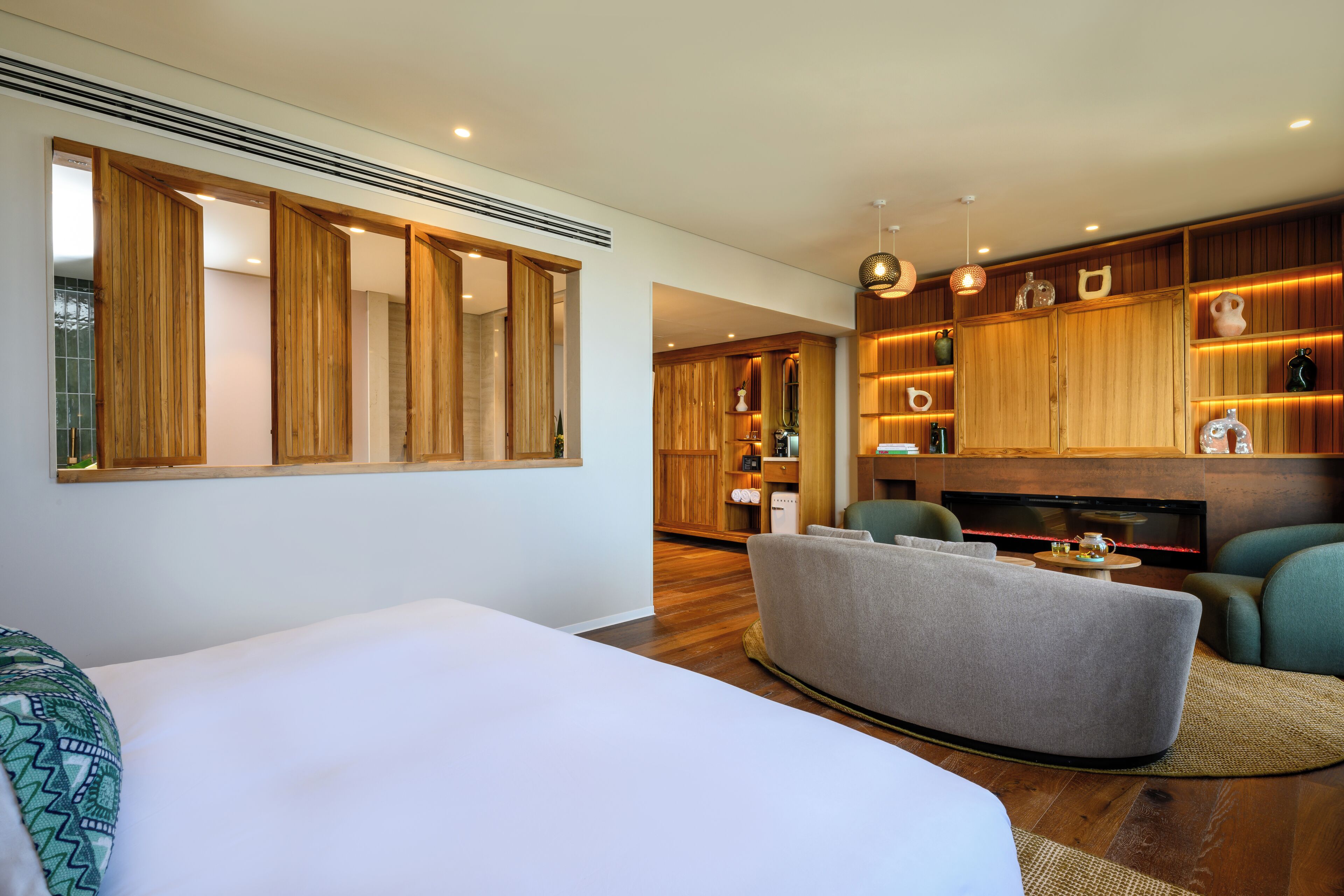 A modern hotel room with a large bed, a seating area with a sofa and armchairs, wooden paneling, a television, and a fireplace.