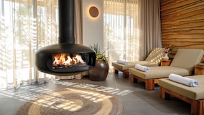 A modern living room with a wood-burning stove, two lounge chairs, a large potted plant, and a decorative wall panel. - Canaan Hotel - Limited Edition By Fattal (Safed)