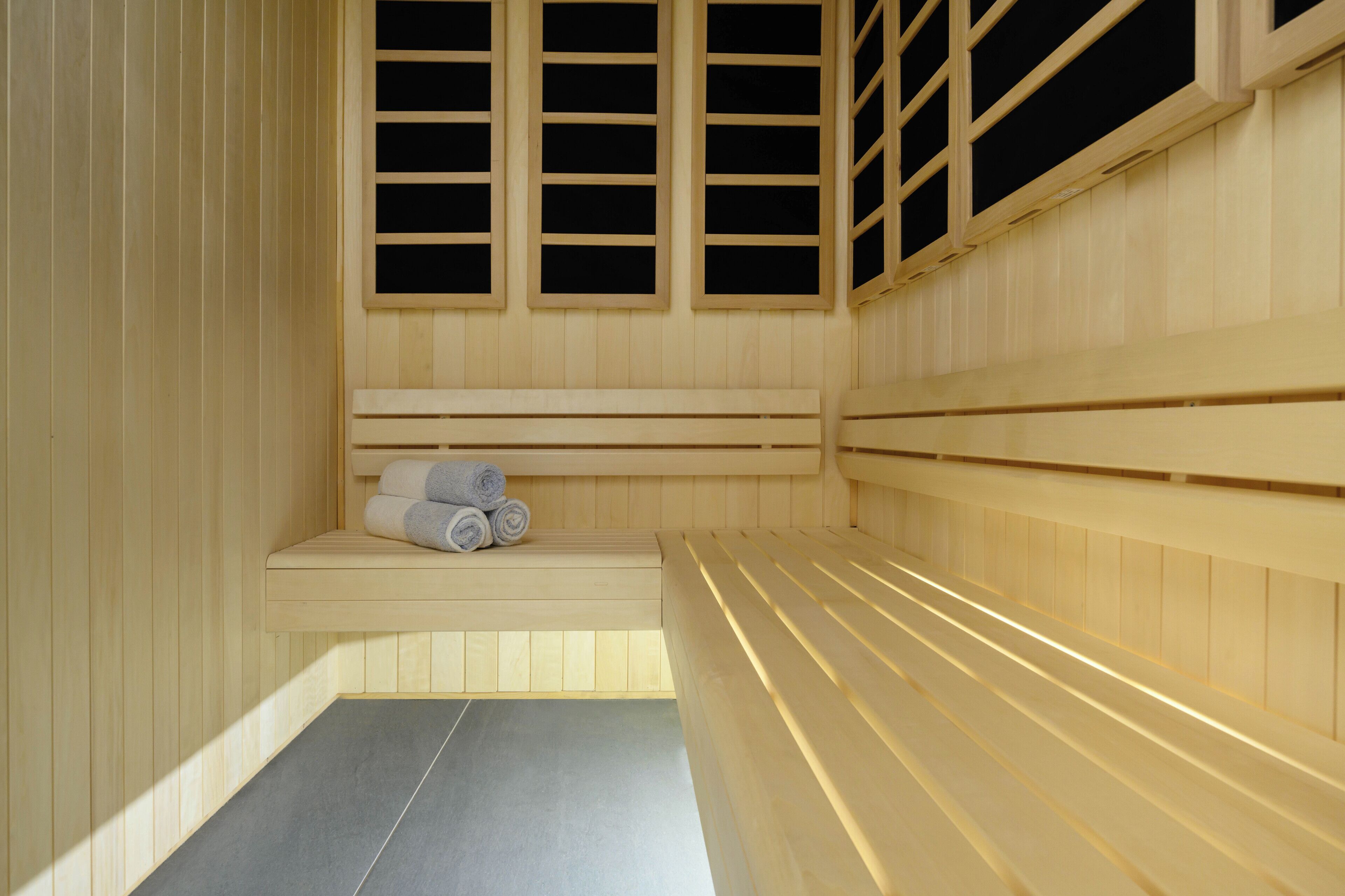 Una sauna con bancos de madera, un banco con toallas y una ventana con persianas.