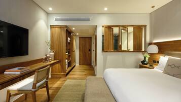 A modern hotel room with a large bed, a desk with a chair, a TV, a wardrobe, and a mirror.