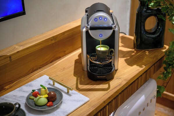 Una cafetera sobre una encimera de madera con un plato de fruta y una taza de café.