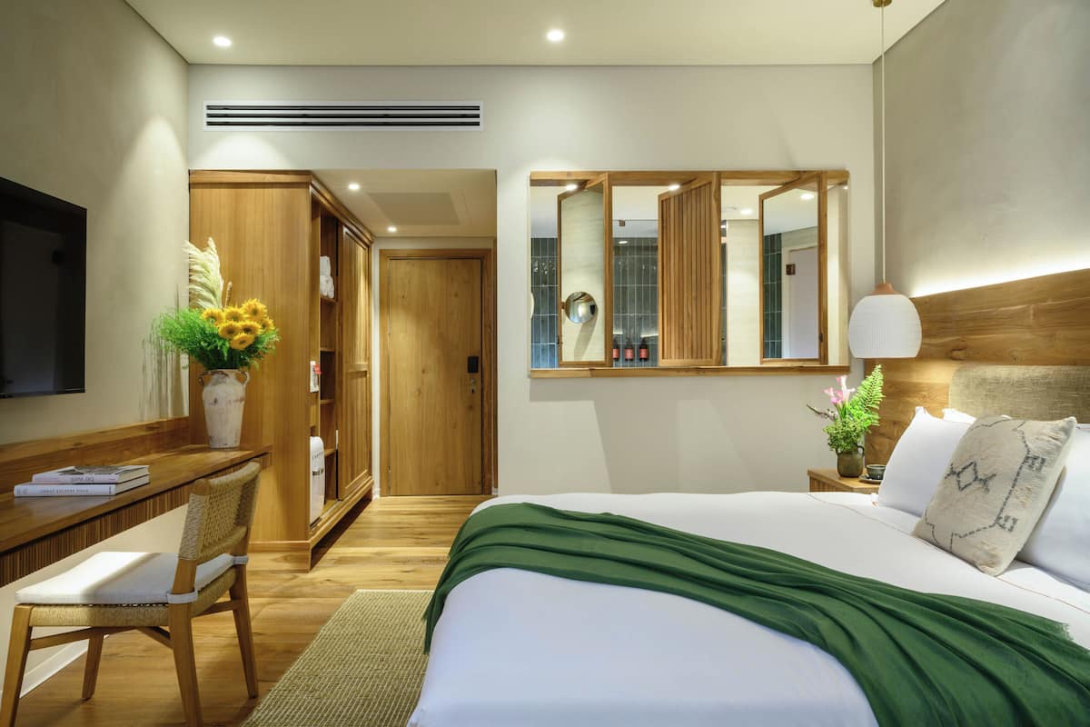 A hotel room with a bed, a desk, a chair, a mirror, and a window.