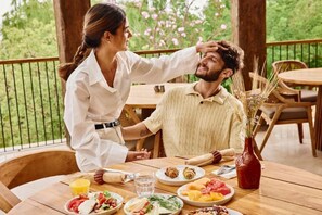 Un coin repas avec une table dressée pour deux personnes, un vase contenant des plantes séchées et une vue sur la verdure.