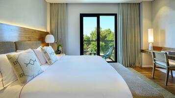 A hotel room with a large bed, a desk, and a view of greenery through the window.