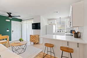 Une cuisine moderne avec des meubles blancs, un tabouret de bar en bois et un coin repas comprenant une table et des chaises.
