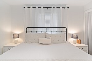 A neatly made bed with a black metal headboard, white bedding, and striped pillows. There are two bedside tables with lamps and a small wooden box on one.