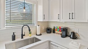Eine moderne Küche mit weißen Schränken, einer Edelstahl-Spüle, einer hängenden Pendelleuchte und einer Kaffeemaschine.