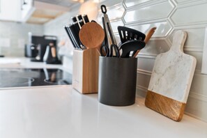 Eine Küchenarbeitsplatte mit einem Besteckhalter, der verschiedene Küchenwerkzeuge, ein Schneidebrett und im Hintergrund eine Kaffeemaschine enthält.
